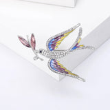 Multicolor dove brooch with layered wing colors in yellow, pink, and blue, pink leaf elements, and clear stones, front view on white squares in studio.