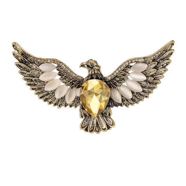 Eagle brooch with gold-tone metal, large yellow faceted center stone, and white accent stones, cutout on white.