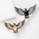 Pair of eagle brooches with gold-tone and silver-tone finishes, yellow and black faceted center stones, and white oval beads as accents. Flat lay on white surface.