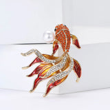 Fish brooch set in gold-tone metal with orange stones, red enamel fins, clear accents, and imitation pearl, upright studio pose.