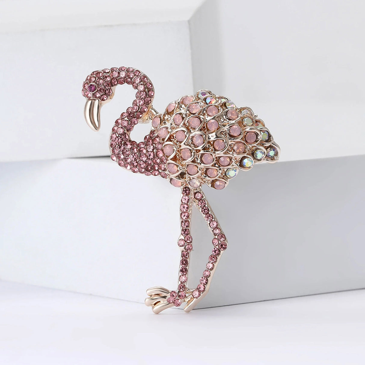 Flamingo brooch with pink faceted stones and iridescent round accents on the body, upright pose on white surface.