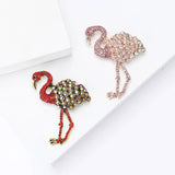 Set of two flamingo brooches with red and pink-tone stones and multicolor accents, flat lay on white surface.