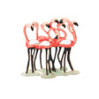 Flamingo brooch featuring group of red-tone birds with white wings and black legs on a green base, cutout on white.