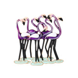 Flamingo brooch showing group of purple birds, with white wings, and black legs on green-blue base, cutout on white.