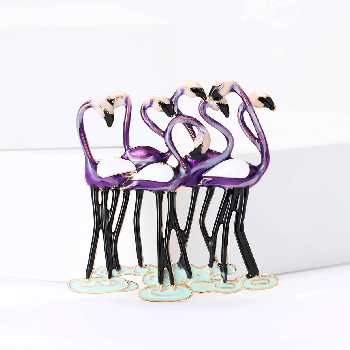 Flamingo brooch with group of purple birds, featuring black legs and white wings, shown on white platform.