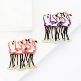 Two flamingo brooches with grouped pink-red and purple birds, featuring black legs and white wings, flat lay on white surface.