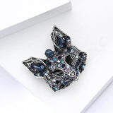Fox brooch in silver-tone metal with stones in multiple shades of blue and black eyes, angled view on white block.