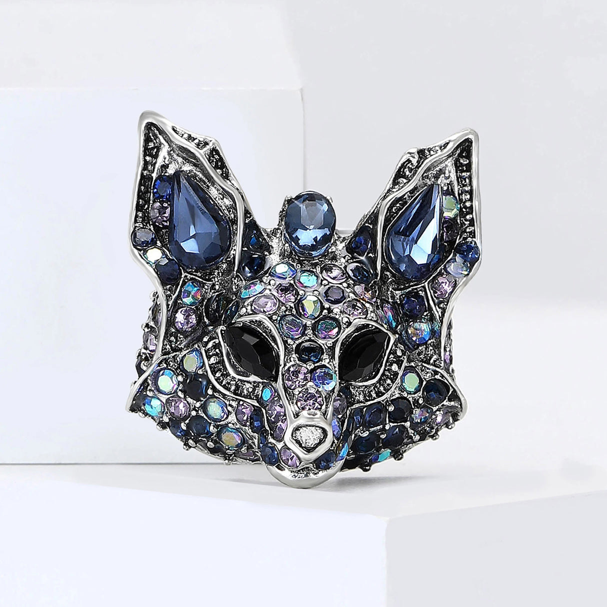 Fox brooch with silver-tone base, blue faceted stones, iridescent accents, and black eyes, upright pose on white block.