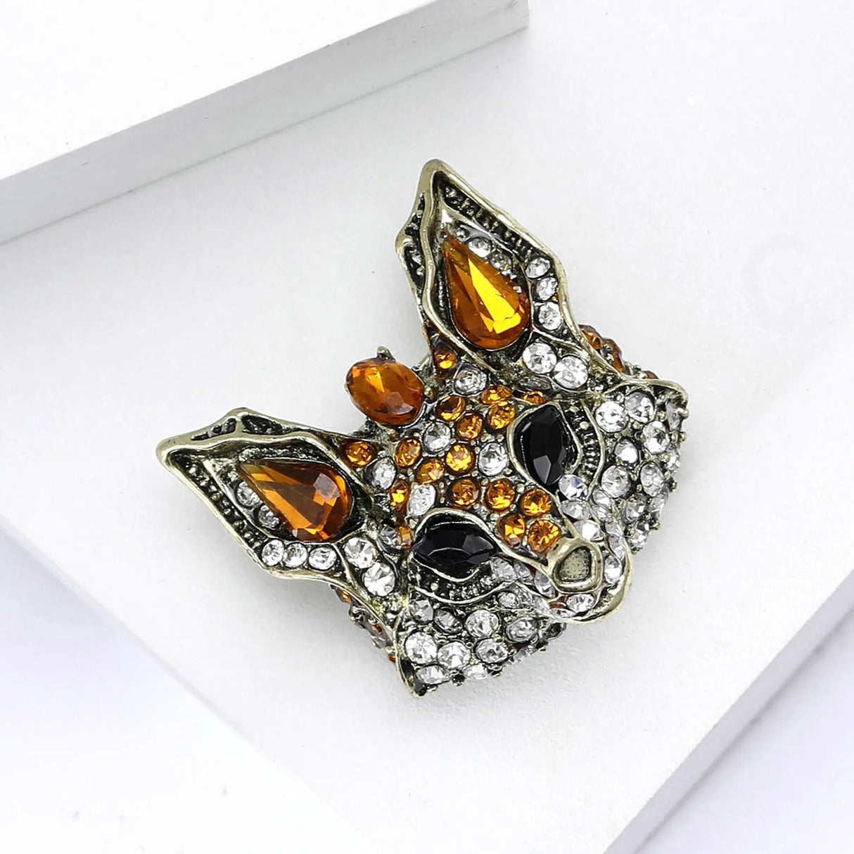 Fox brooch with orange teardrop stones, clear round accents, and black eyes, angled view on white platform.