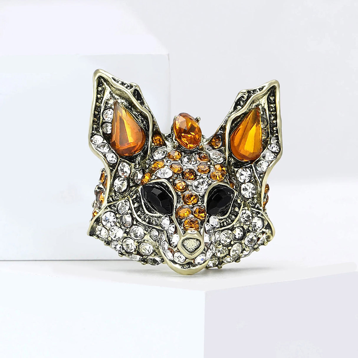 Fox brooch with orange and clear faceted stones, and black eye details, upright on white block.