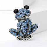 Frog brooch with silver-tone base, covered in small blue round stones, and large black eyes, upright pose on white in studio.