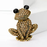 Frog brooch with gold-tone base, clustered light brown stones, and black faceted eyes, upright pose on white studio backdrop.