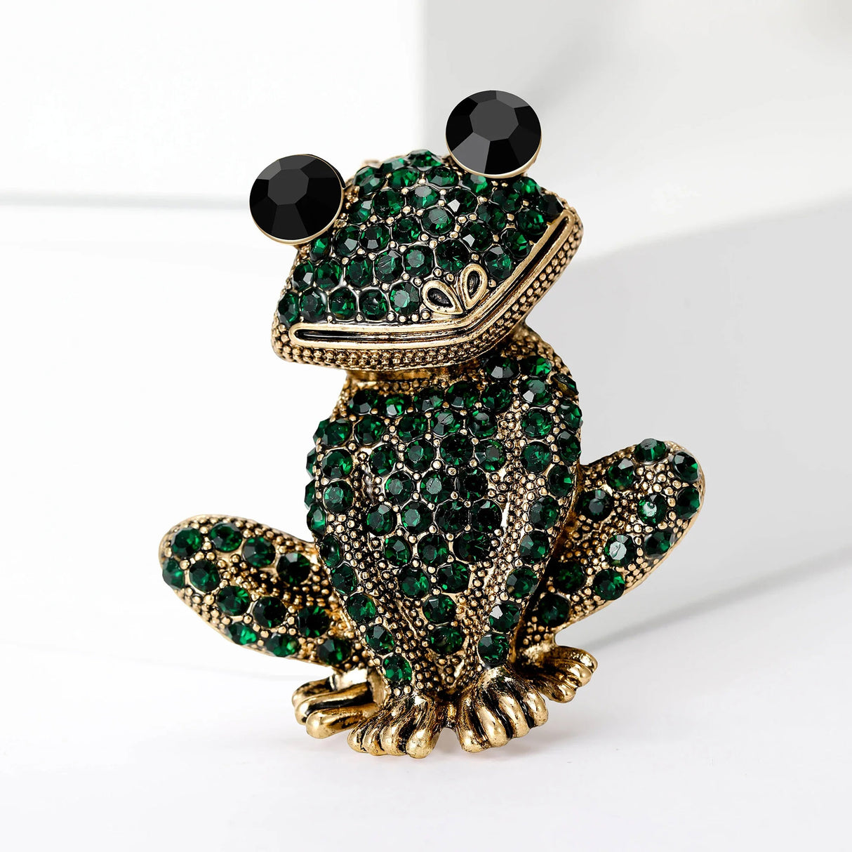 Frog brooch with gold-tone metal finish, dark green faceted stones, and black eyes, upright studio pose.