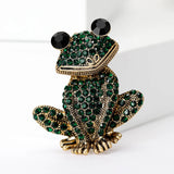 Frog brooch with gold-tone metal finish, dark green faceted stones, and black eyes, upright studio pose.