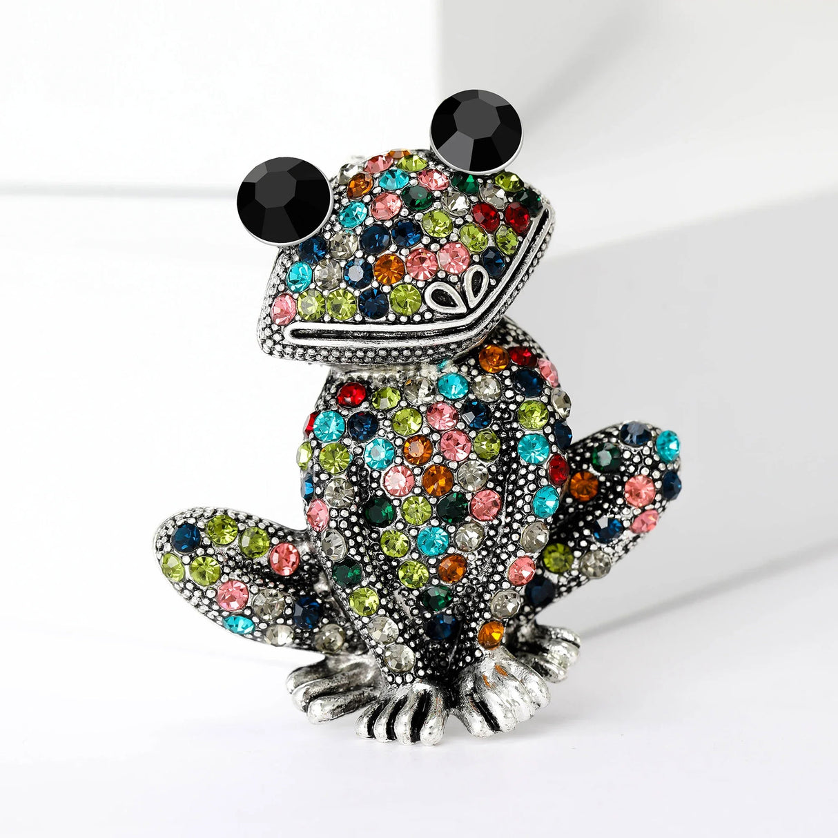 Frog brooch with silver-tone base, multicolor faceted stones, and large black eyes, upright pose on white.