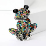 Frog brooch with silver-tone base, multicolor faceted stones, and large black eyes, upright pose on white.