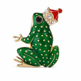Green enamel frog brooch with gold-tone detailing, black eye, and red crown with clear faceted stones, cutout on white background.