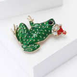 Frog brooch featuring a green enamel body with raised gold-tone dots, black eye, and red crown with clear stones, angled top-down view.