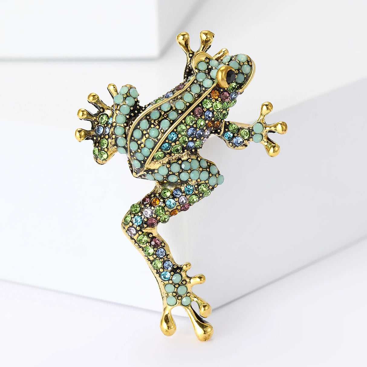 Frog brooch in climbing pose with gold-tone metal base, turquoise and multicolor stones, upright studio view on white.