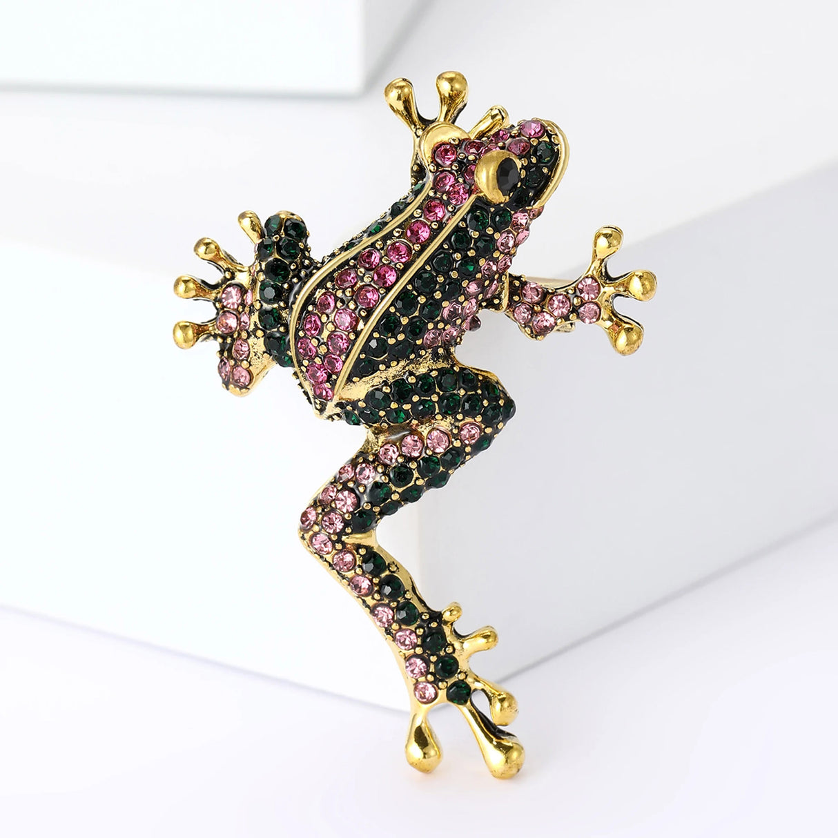 Frog brooch in gold-tone metal finish with pink and dark green faceted stones, upright pose on white background.