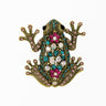 Frog brooch with gold-tone metal finish, adorned with pink, teal, and iridescent faceted stones, cutout on white background.