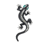 Gecko lizard brooch with silver-tone body, clear and dark faceted stones, and green-toned eyes, cutout on white background.