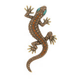 Gecko lizard brooch with bronze-tone metal finish, orange and beige faceted stones, and green eyes, cutout on white.