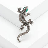 Gecko lizard brooch with smoky grey faceted stones and green eyes, angled studio view on white.