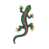 Gecko lizard brooch with teal body, pink faceted center stones, green eyes, and gold-tone claws, cutout on white.