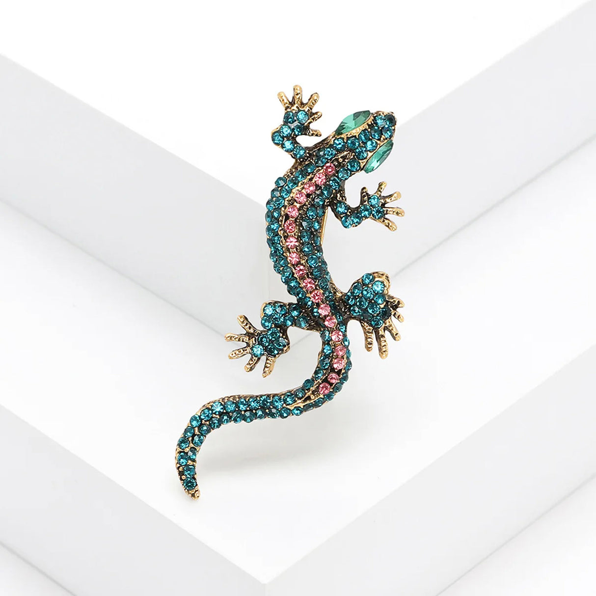Gecko lizard brooch with teal and pink faceted stones, green eyes, and gold-tone detailing, angled view on white background.