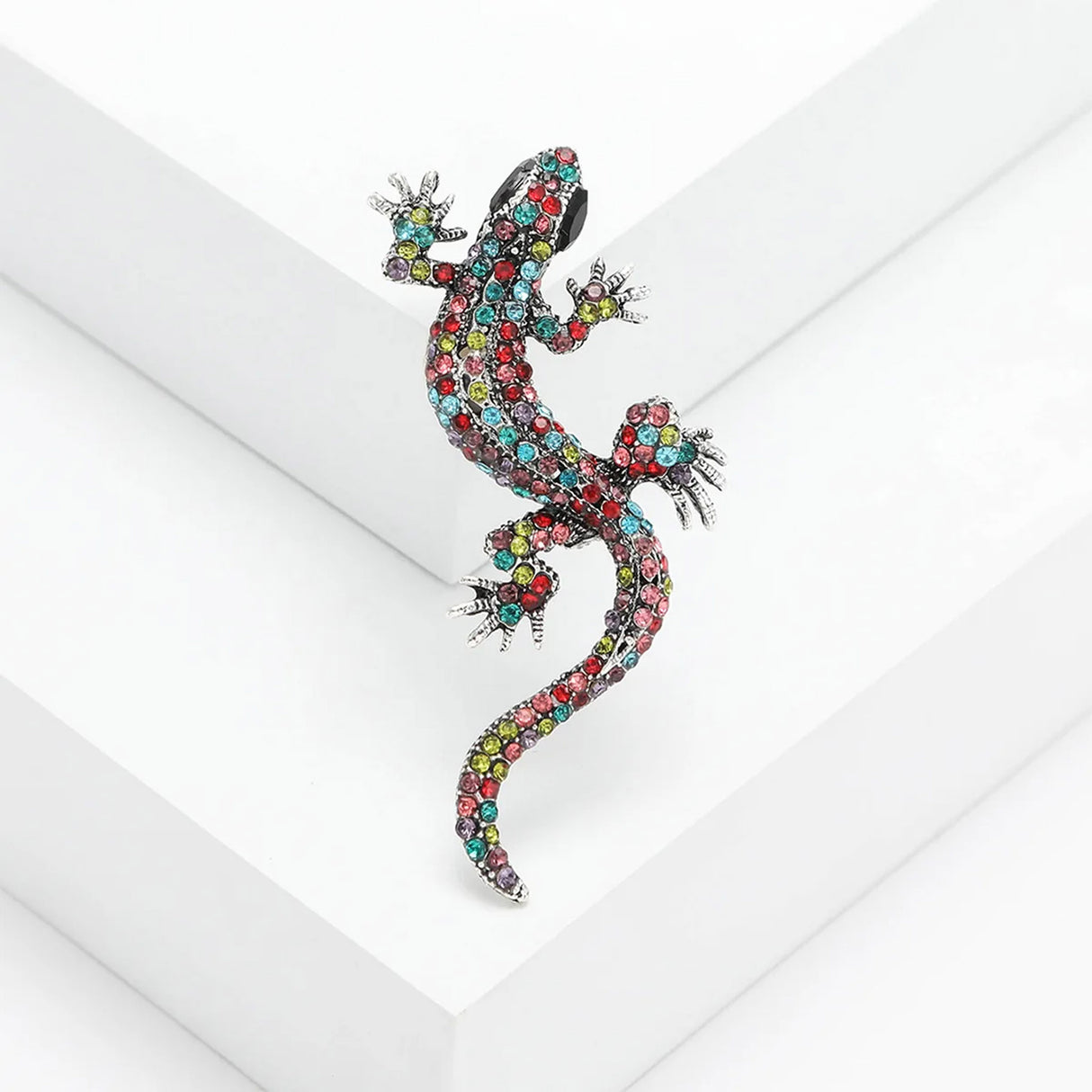 Gecko lizard brooch with multicolor faceted stones and silver-tone claws, angled on white studio backdrop.