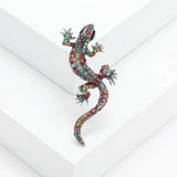 Gecko lizard brooch with multicolor faceted stones and silver-tone claws, angled on white studio backdrop.