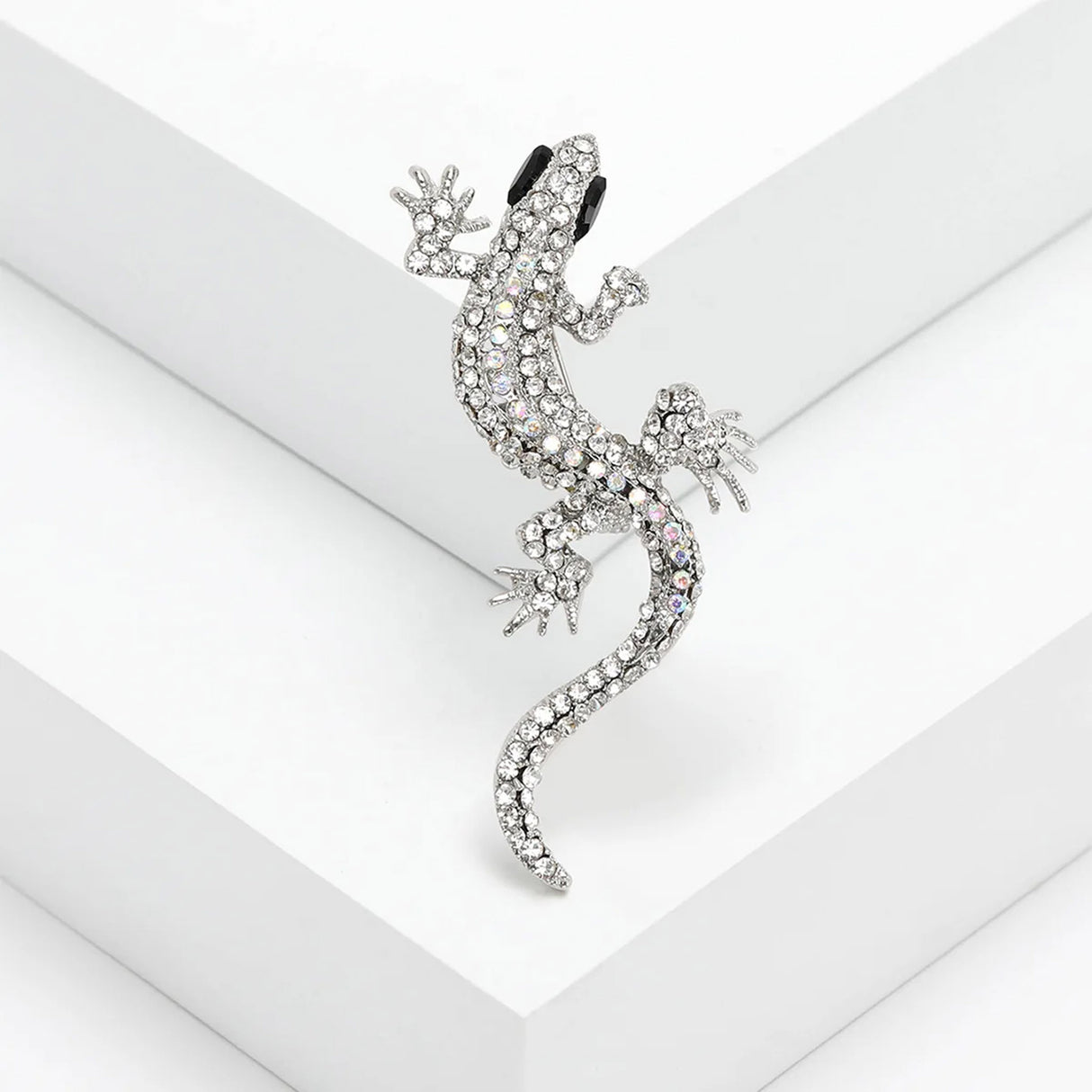 Gecko lizard brooch with clear faceted stones, black eyes, and silver-tone claws, angled studio view on white surface.