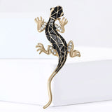 Lizard brooch in gold-tone metal finish with black patterned enamel and clear stones, standing on white block.