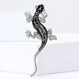 Lizard brooch in silver-tone metal with black enamel geometric design and clear stones, standing on white block.