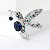 Hummingbird brooch with silver-tone finish, blue faceted center stone, multicolor decorative stones, front view on white.