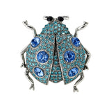 Ladybug brooch with silver-tone metal, blue faceted stones, and black eyes, cutout on white.