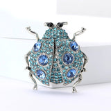 Ladybug brooch with silver-tone metal, blue faceted stones, and black eyes, upright pose on white block.