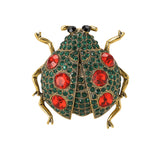 Ladybug brooch with gold-tone metal, green base, red faceted stones, and black eyes, cutout on white.