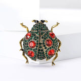  Ladybug brooch with gold-tone metal, green base, red faceted stones, and black eyes, upright pose on white block.