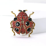 Ladybug brooch with gold-tone metal frame, red faceted stones, black decorative spots, and black eyes, upright front view on white block.