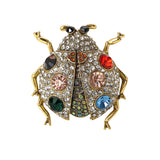Ladybird brooch with gold-tone metal, clear faceted stones, multicolor accents, and black eyes, cutout on white.