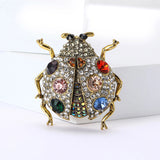 Ladybug brooch with gold-tone metal, clear base, multicolor faceted stones, and black eyes, upright front view on white block.