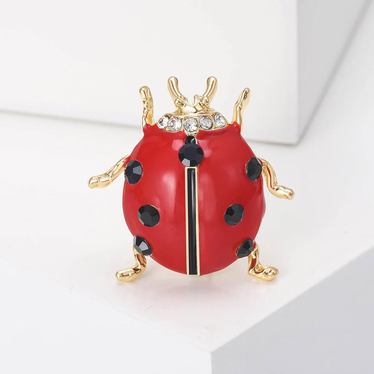 Ladybug brooch with red enamel body, black faceted spots, small clear stones on head, and gold-tone legs, upright view on white.