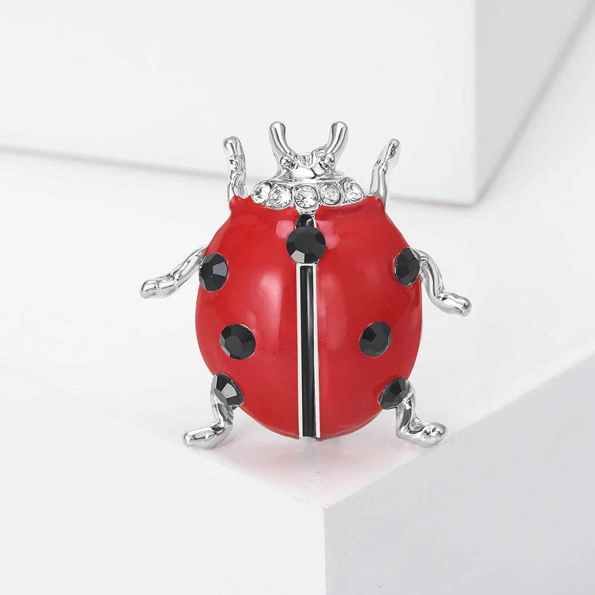 Ladybird brooch with red enamel shell, black faceted spots, clear accent stones, and silver-tone legs, upright view on white.