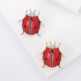 Pair of ladybird brooches with red enamel bodies, black faceted spots, clear accent stones, and silver-tone and gold-tone legs. Top-down studio display on white.