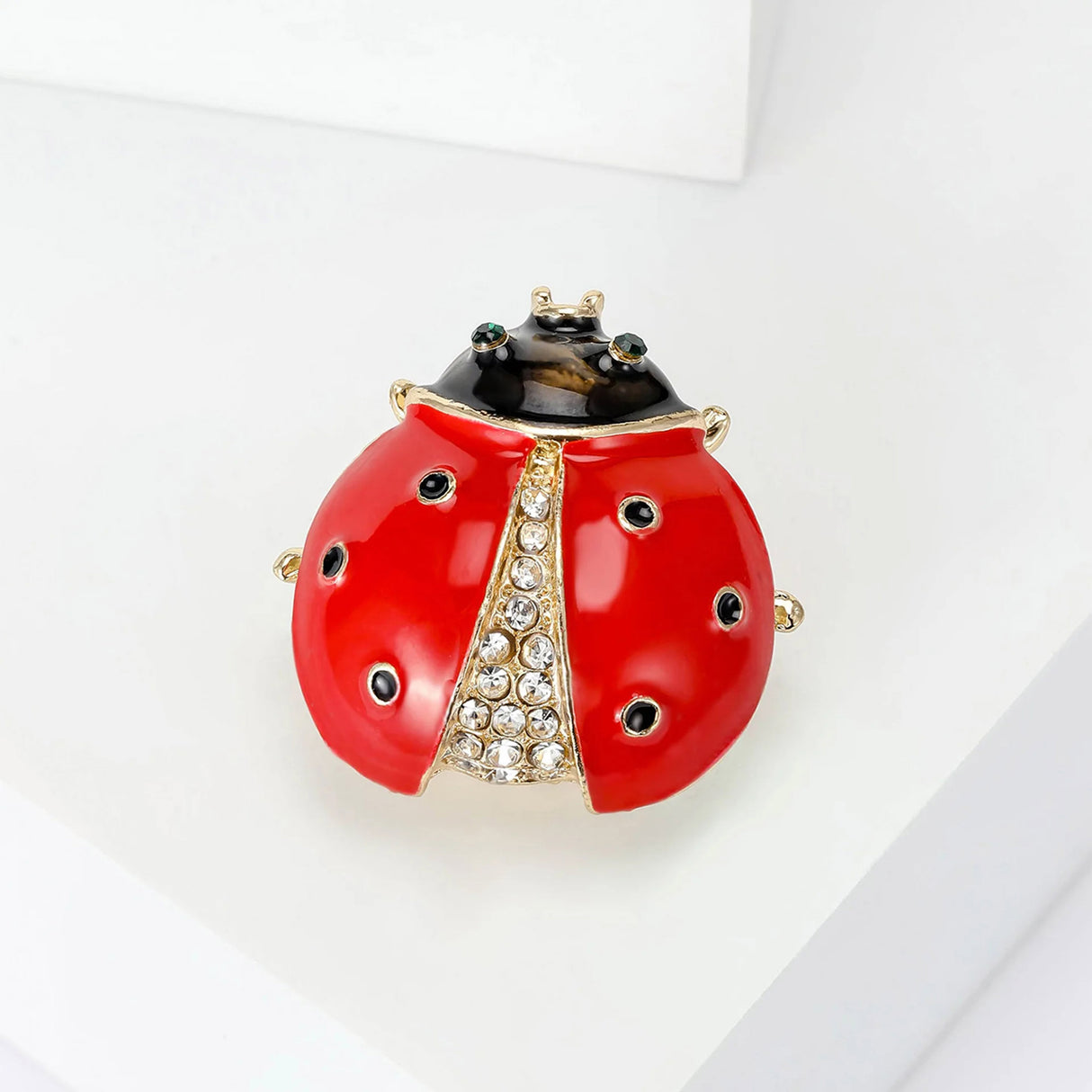 Ladybug brooch with glossy red wings, black head, green eyes, and clear faceted stones, angled pose on white display.