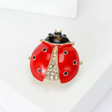 Ladybug brooch with glossy red wings, black head, green eyes, and clear faceted stones, angled pose on white display.