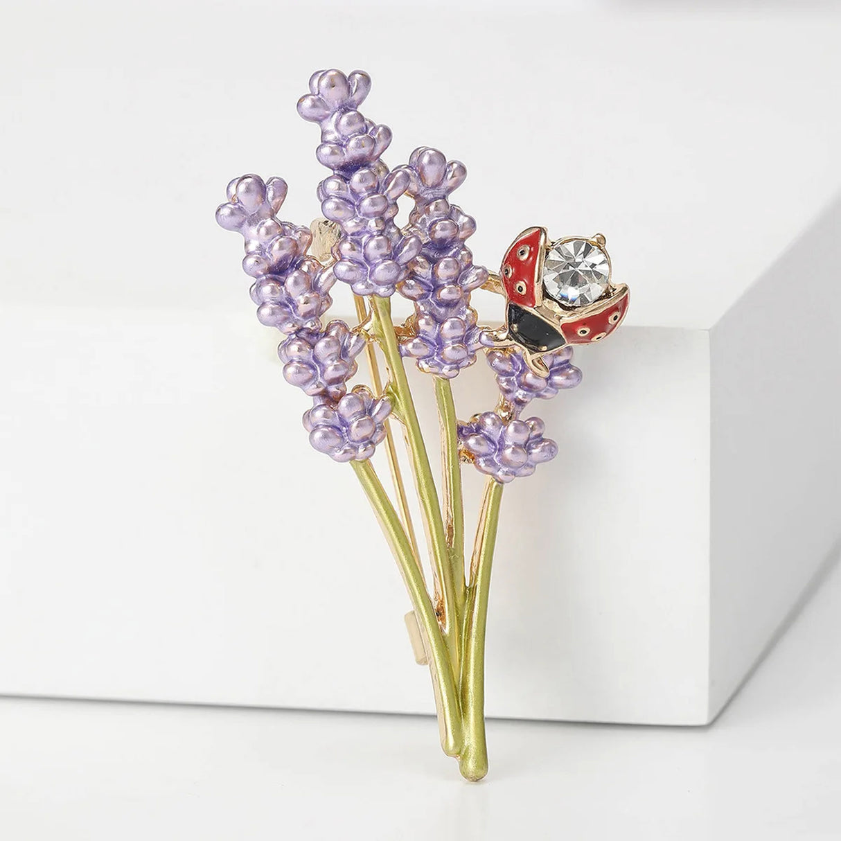 Lavender brooch with purple enamel clusters, gold-tone stems, and red ladybird detail with clear stone, angled studio view.