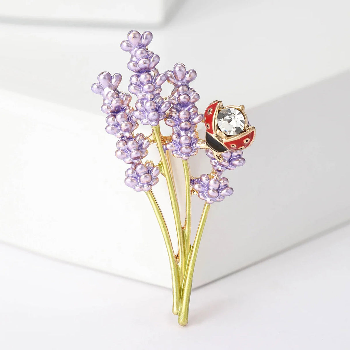 Lavender flower brooch with purple enamel blooms, gold-tone stems, and red ladybird with clear faceted stone, upright pose.